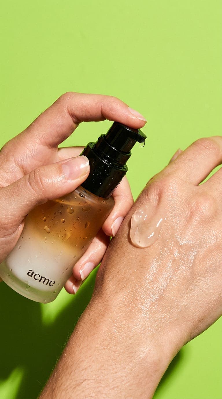 Hand pumping clear Acme gel onto the back of the other hand against a lime backdrop